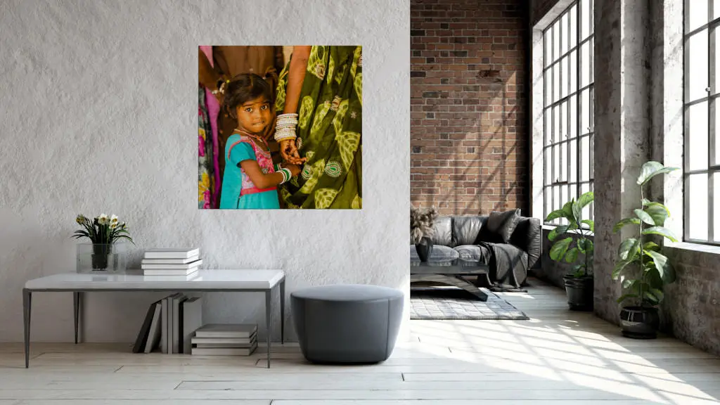 Ein Fotokunstwerk hängt in einem Wohnzimmer. Abgebildet ist ein kleines Mädchen in einem blau-pinken Kleid, welches die Hand der Mutter hält und schaut neugirig.