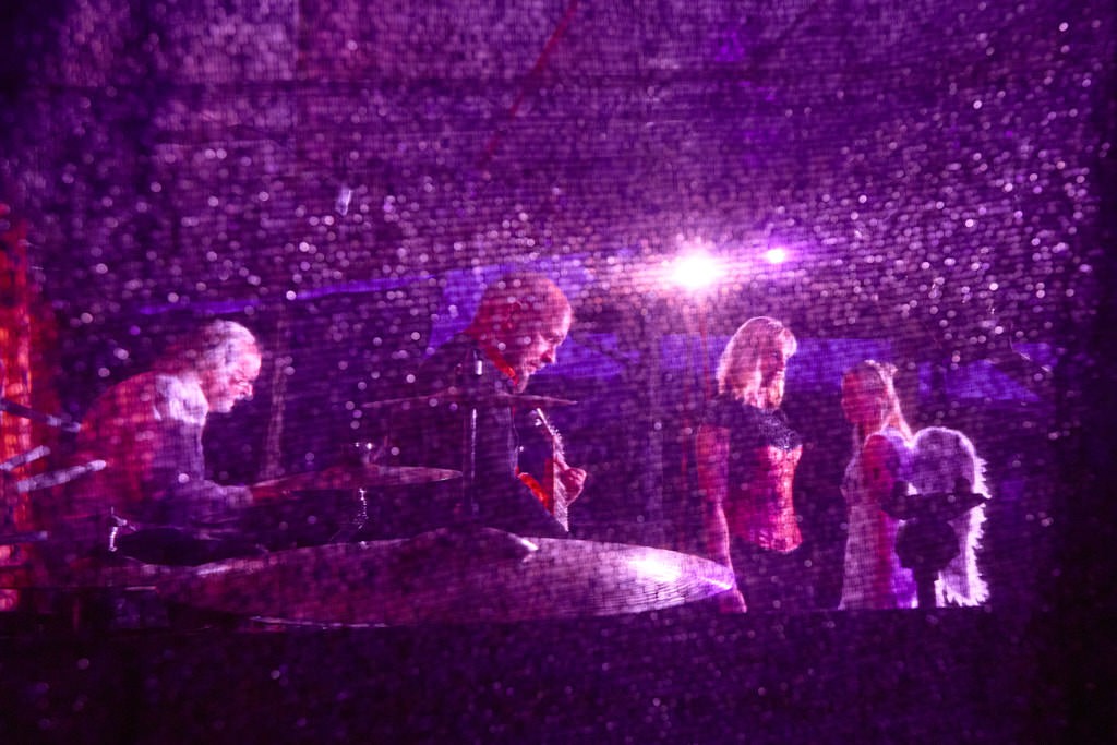 Ein lila farbenes Fotokunstwerk von 4 Personen, die auf einer Bühne stehen.