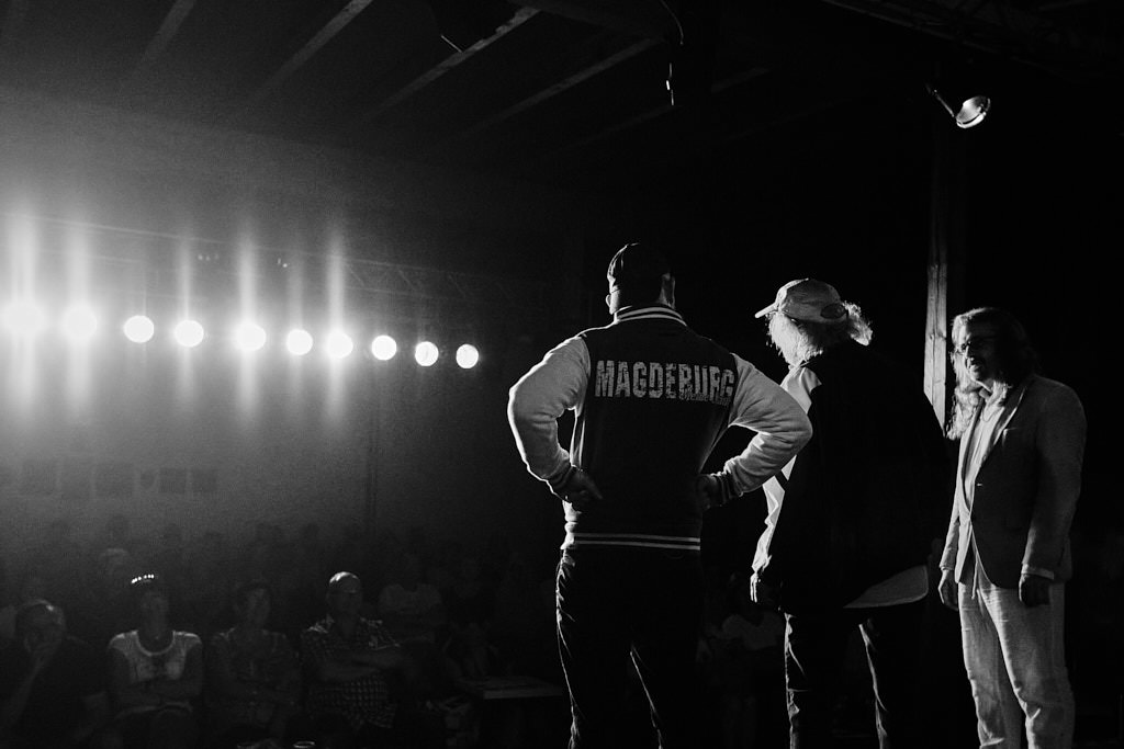 Schwarz-weiß Fotokunstwerk von 3 Männern, die auf der Bühne stehen und in die Menge schauen.