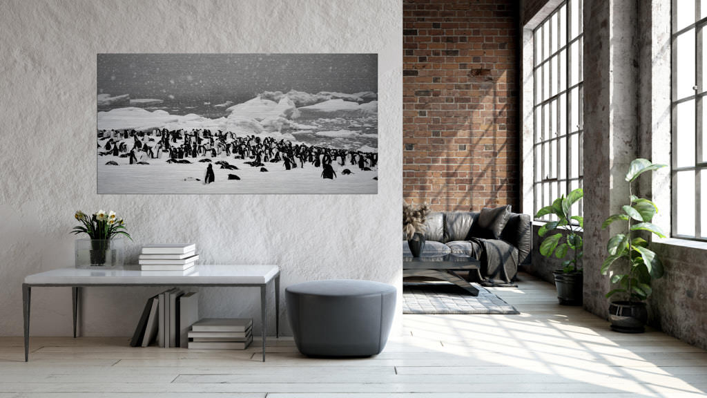 Ein Fotokunstwerk in einem Wohnzimmer mit vielen Pinguinen auf einer großen Schneefläche. Es schneit.