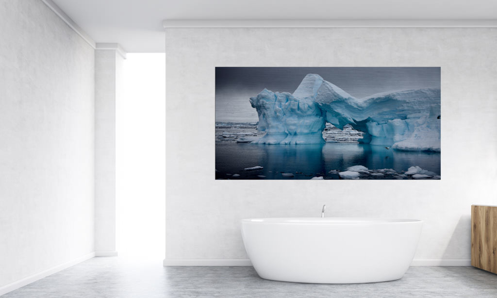 Ein Fotokunstwerk hängt in einem Badezimmer. Abgebildet ist ein Eisberg aus der Antarktis, welcher in der Mitte zusammenbricht.